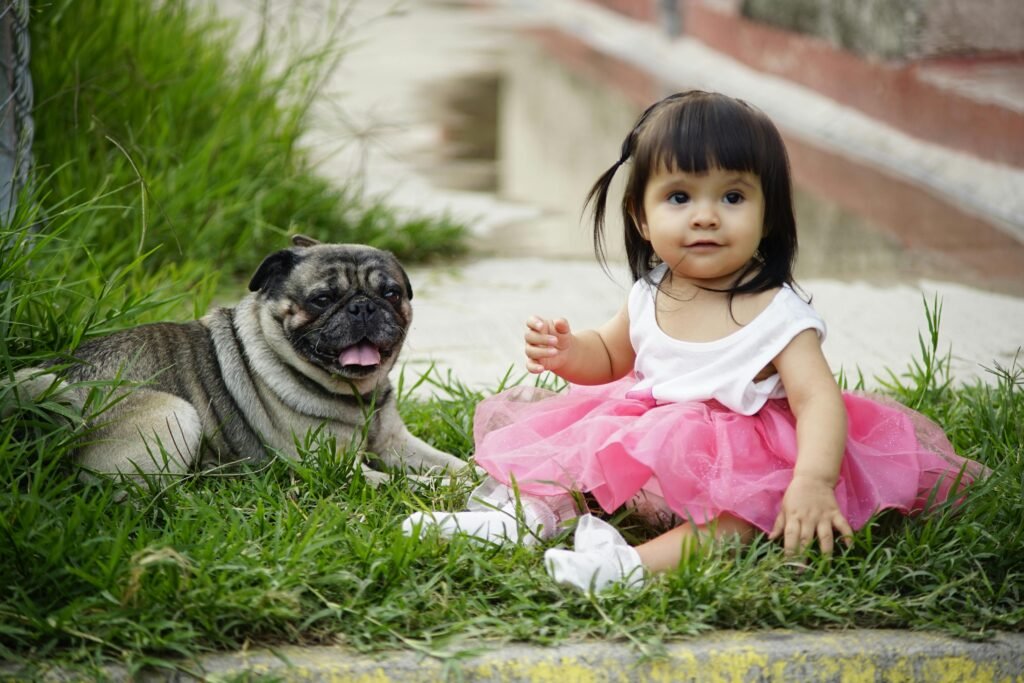 pexels-photo-6031849-6031849 Young child in pink tutu sitting on grass with a pug, showing safe and joyful companionship between dogs and kids