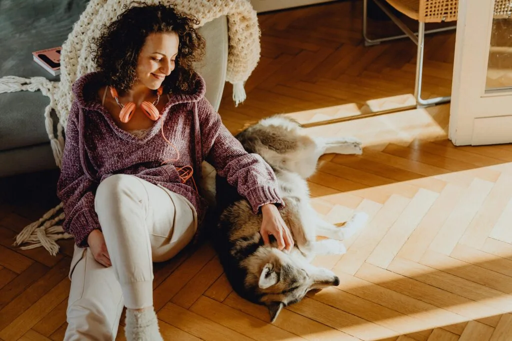 Woman petting her dog while sitting on a wooden floor at home, enjoying a peaceful moment indoors.